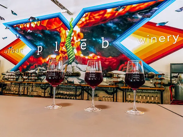 pleb urban winery with 3 glasses of red wine and their urban art mural and logo