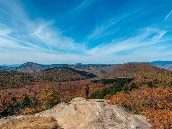 What Is It Like Living in Asheville NC Hiking At Sam Knob with woman wearing a backpack and looking over a cliff