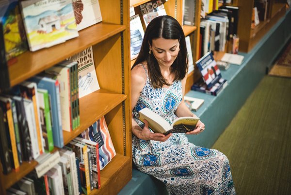 Malaprop's Bookstore in Asheville NC with white brunette women in dress sitting on shelf and flipping through a book