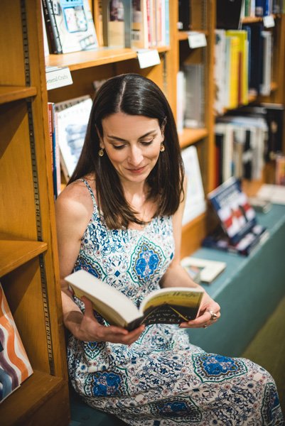 Malaprop's Bookstore Asheville white brunette woman sitting on the corner surrounded by bookshelves and reading Thomas Wolfe's Look Homeward, Angel