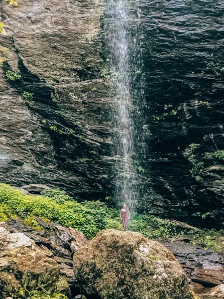 Douglas Falls Waterfalls Near Asheville brunette white woman in a red tank top standing under the falls