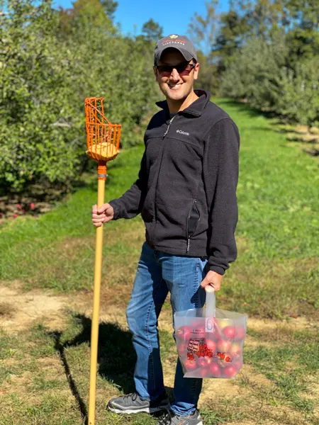 Coston Farm Apple Picking Hendersonville NC with white male in black fleece holding bag full of U-Pick apples and apple picker in apple orchards