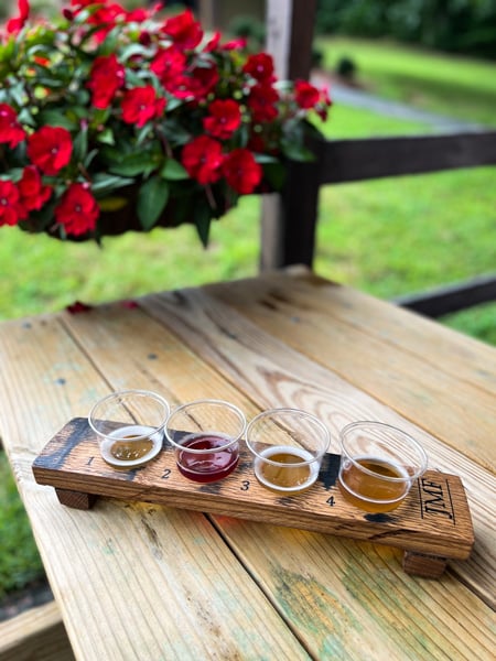 Jeter Mountain Farm Cider Hendersonville NC with flight of yellow and red ciders on picnic table with pink flowers in background