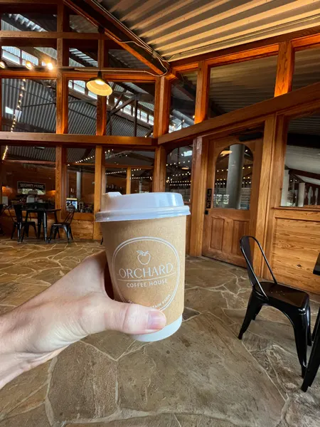 Jeter Mountain Farm Coffee in Hendersonville NC with white hand holding take away coffee cup in front of wooden seating area