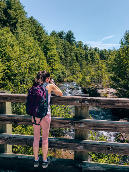 Lake Julia Spillway at DuPont State Recreational Forest with white brunette woman in pink yoga pants and a hiking backpack taking a picture of the mini waterfalls