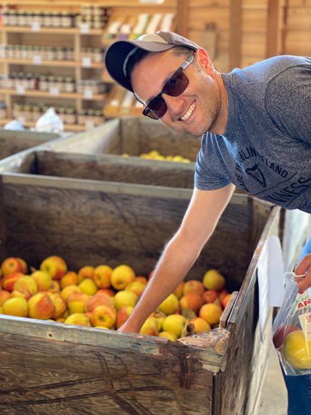 Stepp's Hillcrest Apple Orchard Hendersonville NC with white male in blue shirt with sunglasses and hat reaching into bin of pre-picked apples in farm store