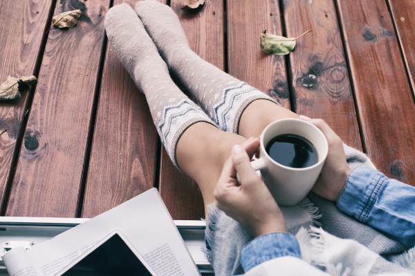 Asheville NC fall reading with white woman wearing long knee-high beige socks, drinking a hot cup of coffee, and sitting next to a pile of books