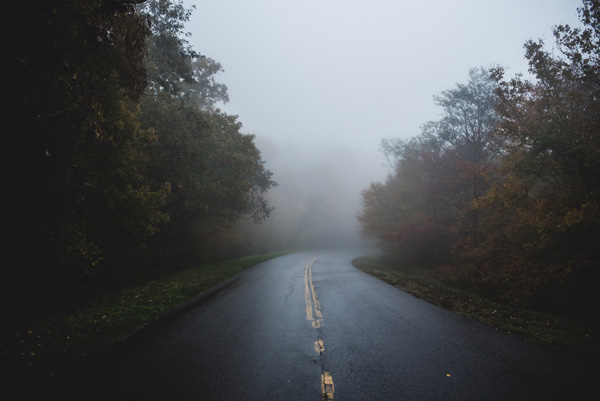 Blue Ridge Parkway Skinny Dip Falls Trail with fog and dark sky with clouds over the two lane road