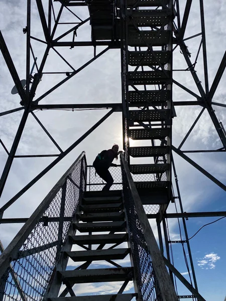 Fryingpan Lookout Tower steel stairs with a woman wearing a hiking backpack going up them
