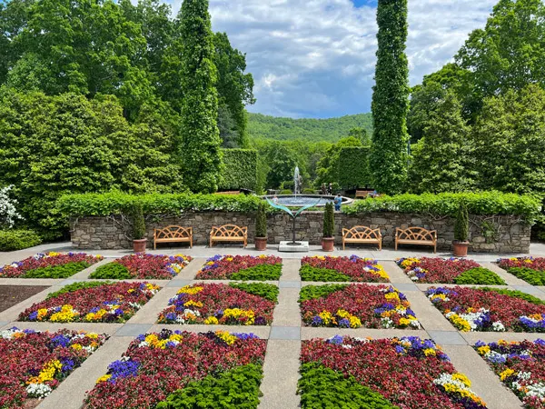 NC Arboretum Quilt Garden with rows of curated flowers in a quilt pattern with trees and fountain in background with blue cloudy sky