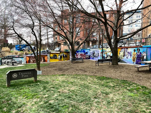 Triangle Park Asheville NC with two walls of murals featuring Black community members and green patch of grass with picnic tables and benches