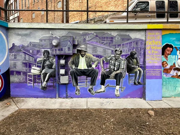 Triangle Park Murals Asheville NC with black and white images of guys sitting in chairs with purple hued buildings behind them