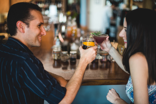 Asheville NC Living Cocktails from Top of the Monk with white male and female doing a cheers with cocktails at a bar