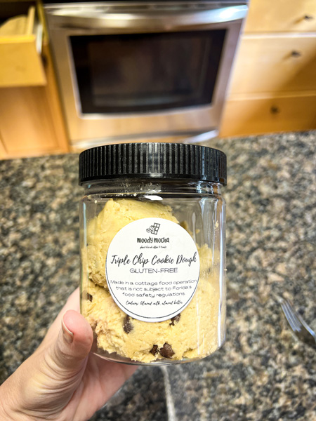 Asheville VeganFest gluten-free cookie dough with white hand holding up container in home kitchen