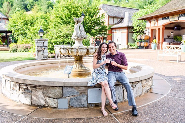 Biltmore Winery in Asheville with white brunette male and woman drinking Biltmore wine sitting in front of a fountain