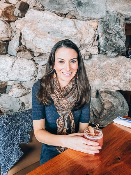 Christine of Uncorked Asheville brunette white woman in a gray dress with a scarf with a cocktail in her hand