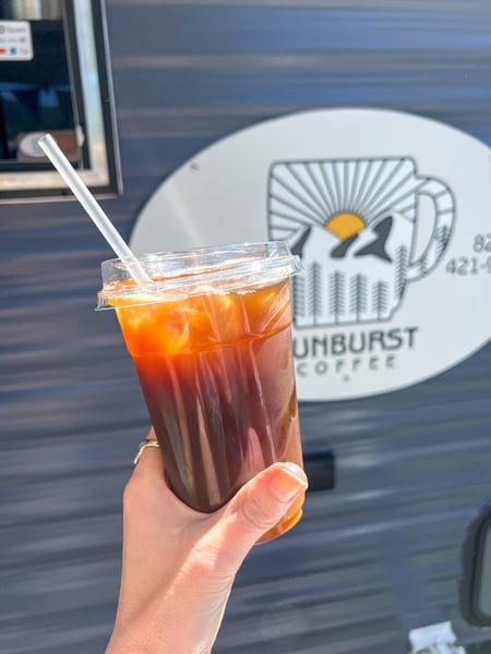 Food Trucks at the Maggie Valley Arts and Crafts Festival, NC with white hand holding up iced coffee in front of Sunburst coffee sign