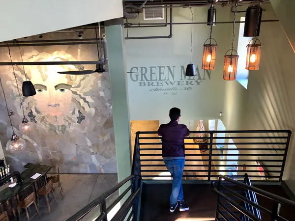 Green Man Brewing In Asheville NC with mural of green man logo and white brunette male looking over railing