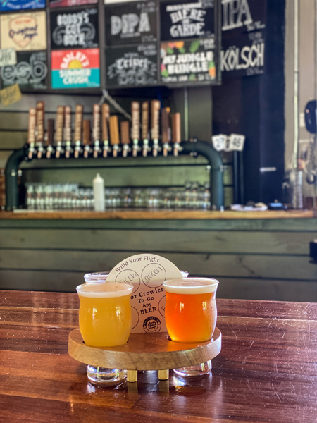 Hillman Beer Historic Biltmore Village with flight of 4 light yellow and orange beers with taproom list blurred in the background