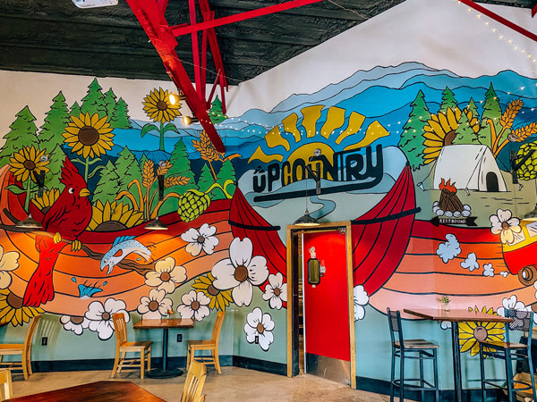 UpCountry Brewing Asheville NC with colorful wall mural with sun, blue mountains and flowers