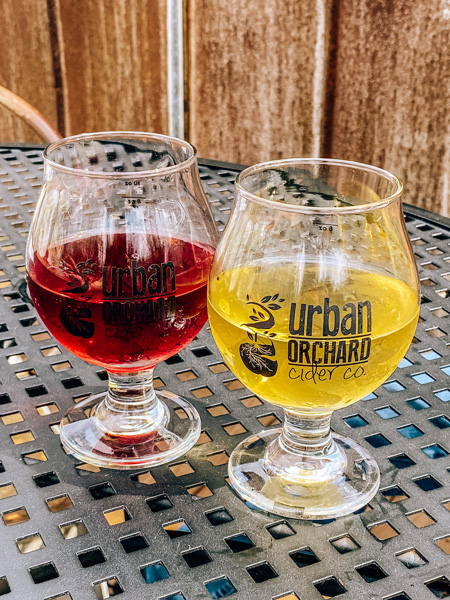 Urban Orchard Cider Co. West AVL with red and yellow cider on a patio table