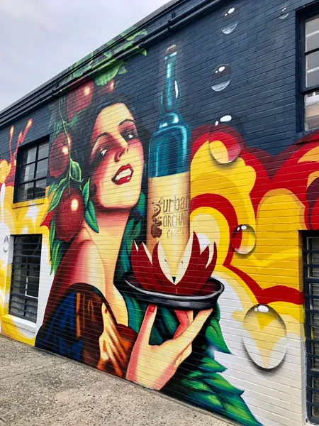 Urban Orchard Cider Company from of the building mural with woman holding bottle of wine on a plate