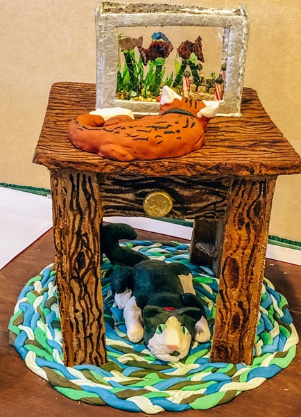 Asheville Winter Events Gingerbread House Competition Grove Park Inn with old fashioned with marshmallow and gingerbread house that looks like a cat laying under a table with a goldfish