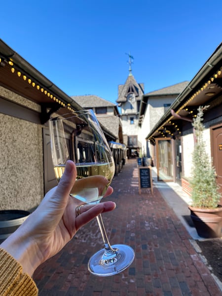Biltmore Estate Winery Clock Tower with white hand holding up a white glass of wine in front of white and brown trimmed clock tower in Antler Hill Village