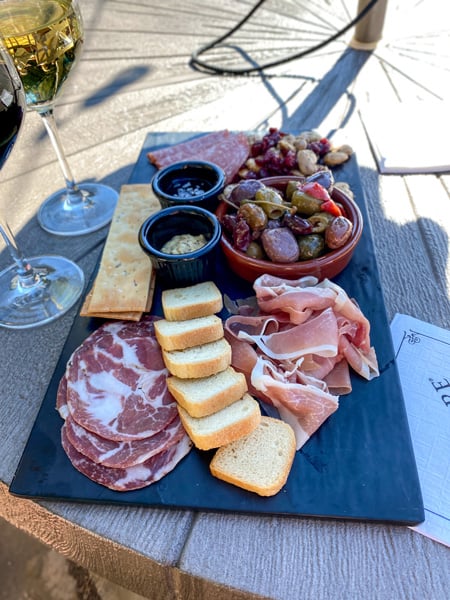 Biltmore Wine Bar Charcuterie Asheville NC with flat black dish filled with small breads, meats, olives, and dips next to red and white wine glasses