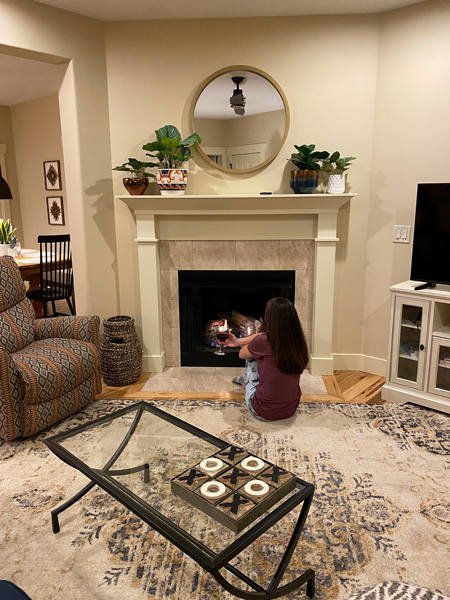 Fireplace at Asheville Cottages with white brunette woman in purple shirt and cat pjs sitting in front of fire with glass of red wine