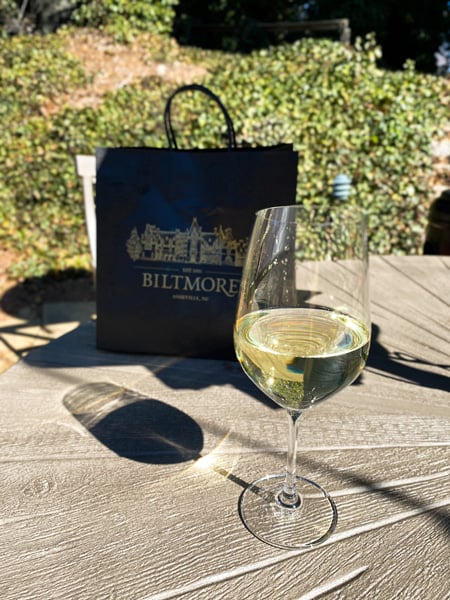 Shopping Biltmore's Antler Hill Village with black shopping back with Biltmore mansion on it and white wine glass on table