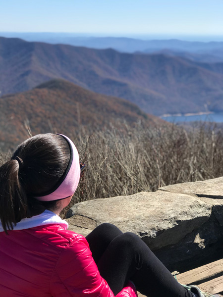 Winter Hikes Asheville NC Craggy Pinnacle with brunette white woman in pink winter coat looking at Asheville watershed