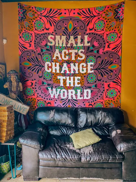 Adam Dalton Distillery Asheville NC with leather couch and tapestry that says Small acts change the world