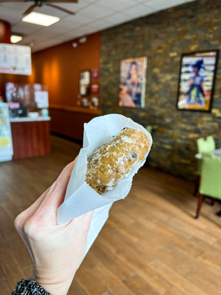 Avas Donuts Asheville NC with white hand holding up a glazed blueberry donut in cafe space with paintings on wall and green chair