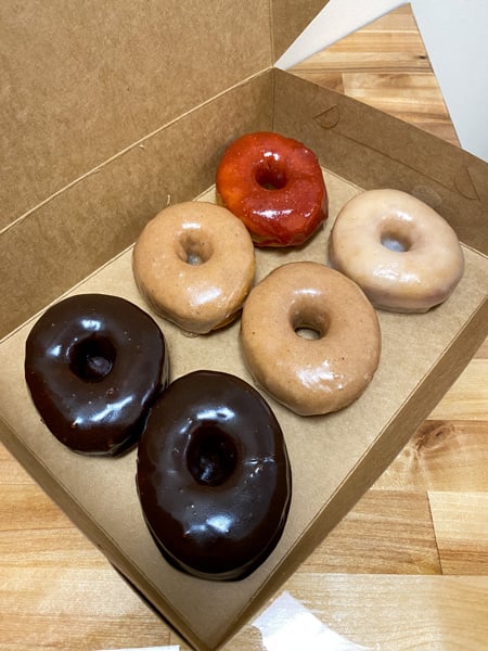 Dough House vegan donuts Black Mountain NC with brown box of a half dozen donuts with two chocolate, two chai, one vanilla, and one strawberry glazed donut
