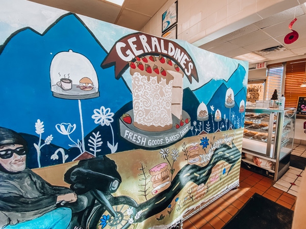 Geraldines Bakery Asheville NC with mural of wedding cake, Blue Ridge Mountains, and man on a motorcycle with bakery in background