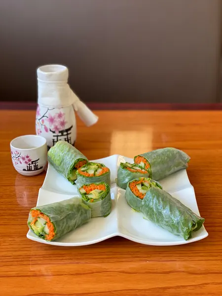 Veggie Summer Rolls with sake at Mr Sushi Asheville. Rolls are filled with avocado, cucumber, and carrots and wrapped in rice paper with sake behind the plate