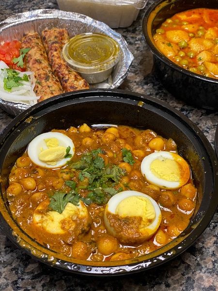 Biryani Express Indian Food Asheville Chickpeas in brown sauce with sliced and cooked eggs and cilantro garnish with kabobs in the background