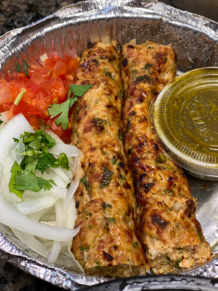 Biryani Express Pakistani and Indian Food Asheville NC with two brown kababs with raw onion, tomato, and green sauce in silver takeout container