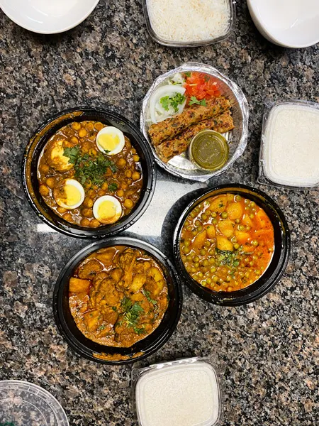 Biryani Express Takeout Asheville NC with four takeout containers with Indian food like chana masala, aloo gobi, and aloo mutter surrounded by more containers of white rice on marble countertop