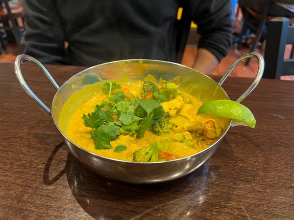 Blue Cream Curry House Asheville NC with image of silver bowl with handles filled with yellow curry, cilantro, and lime garnish on brown table