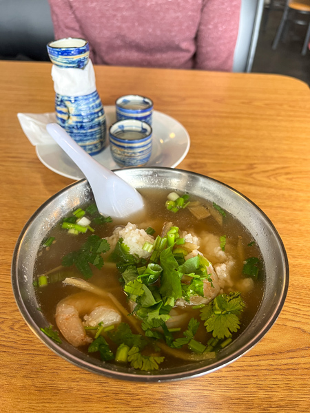 Boon Choo Flat Rock NC Ginger Soup in tin bowl on brown table and garnished with cilantro with hot sake glasses in background