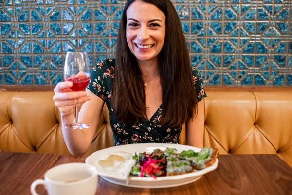 Downtown Asheville Restaurants Tupelo Honey Cafe Brunch with white brunette woman holding up a champagne cocktail and eating a plate of eggs and toast