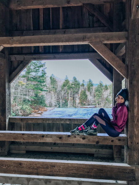 High falls covered bridge DuPont State forest with brunette white woman dressed for winter with a hat sitting on bridge