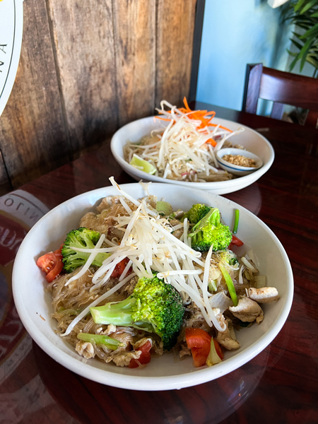 Little Bee Thai Asheville NC with two white bowls filled with Pad Thai and Pad Woon Sen with bean sprouts on top and bowl in front has tomatoes and broccoli