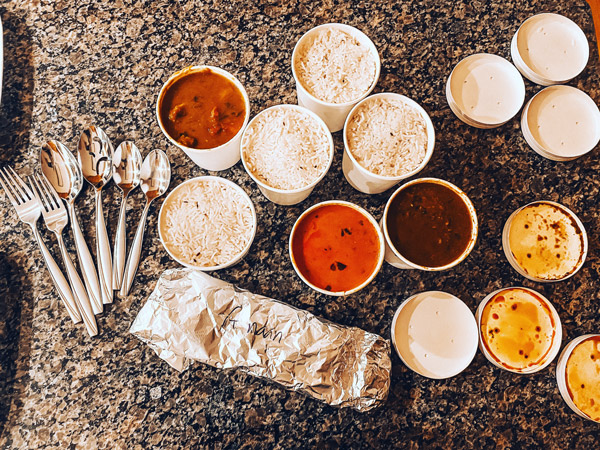 Mela Asheville Indian food takeout containers with white rice, silverware, daal, tandoori chicken, and chicken tikka masala