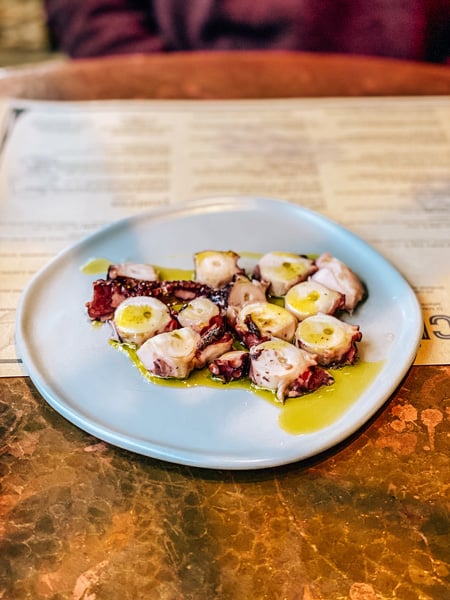 Grilled and cut up Octopus on white plate with olive oil at Curate Restaurant in Downtown Asheville