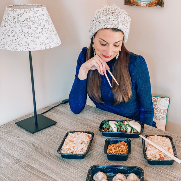 Red Ginger Dimsum and Tapas Asheville takeout with white brunette woman wearing a white hat and holding chopsticks with rice, dumplings and takeout containers