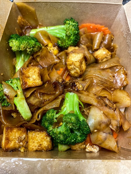 Thai Kitchen Asheville NC with brown takeout box filled with broccoli, thick brown noodles, carrots and tofu