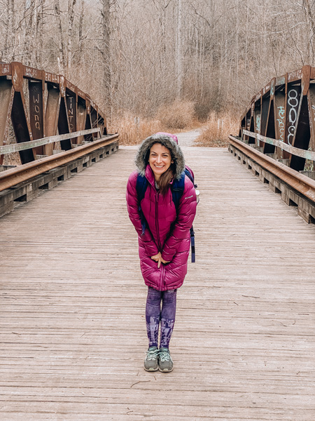 Winter Hikes Near Asheville Daniel Ridge Loop and Falls with brunette white woman in plum coat standing on a bridge